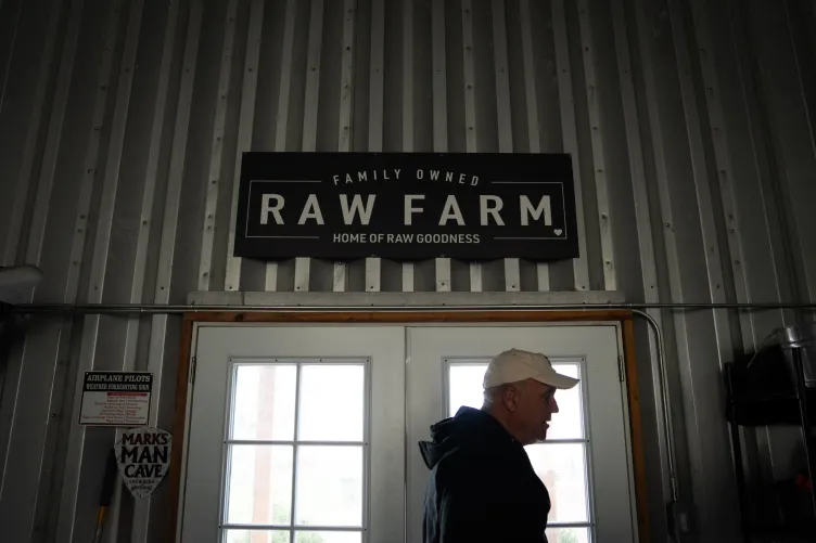 Un homme portant une casquette de baseball sort d'une double porte blanche sous une grande enseigne Raw Farm.