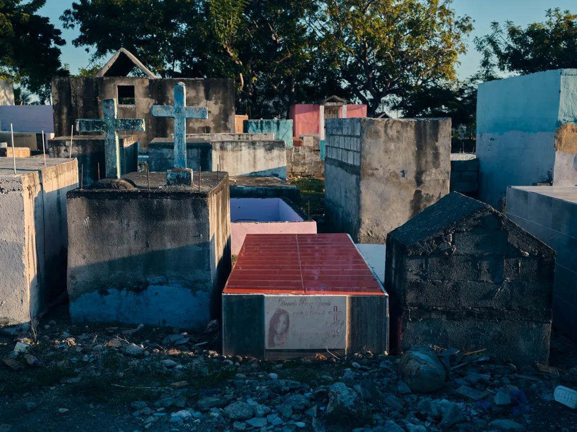 Des tombes en béton en forme de boîte et des croix de pierre se dressent étroitement les unes contre les autres dans un cimetière extérieur sous la lumière du soleil.