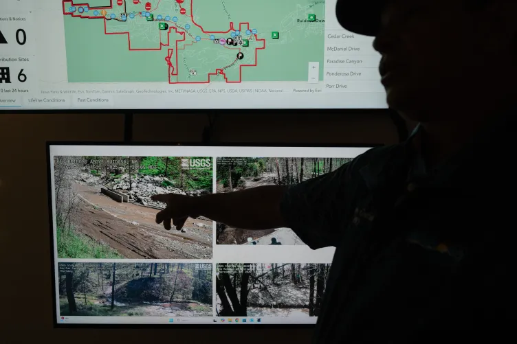 Un responsable pointe du doigt des écrans numériques montrant des cartes et des flux de surveillance des rivières en temps réel de l'US Geological Survey.